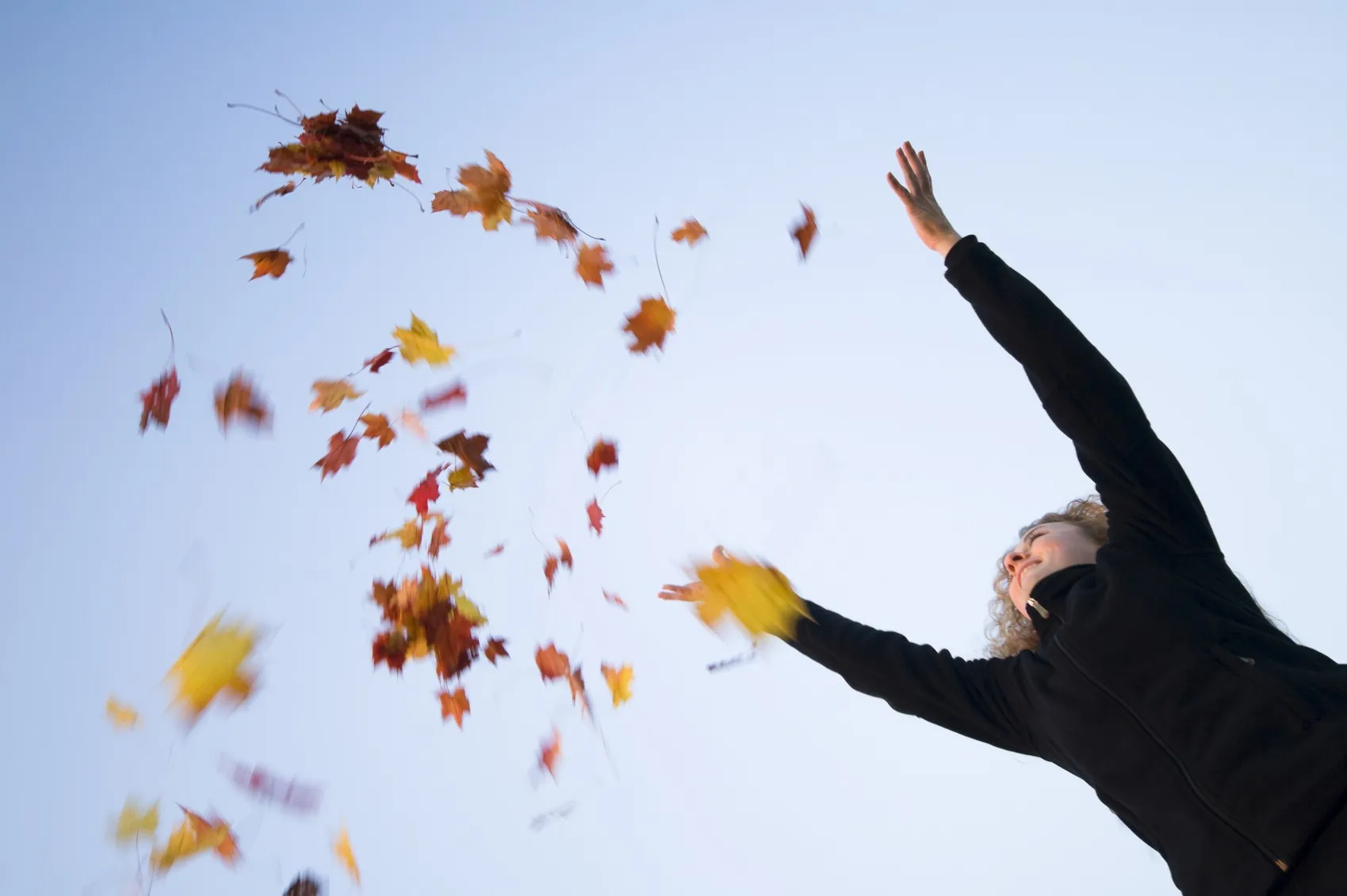 Person wirft Herbstlaub in den blauen Himmel